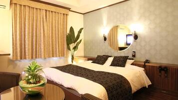 Habitación de hotel con una cama grande, un espejo redondo, una planta en maceta y una mesita.