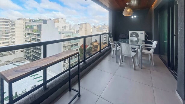 Ein Balkon mit einer hölzernen Bank, einem Glastisch und Stühlen sowie Blick auf die Stadtlandschaft.