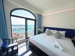 A hotel room with a large bed, a view of the sea, a balcony with a railing, and a chair.