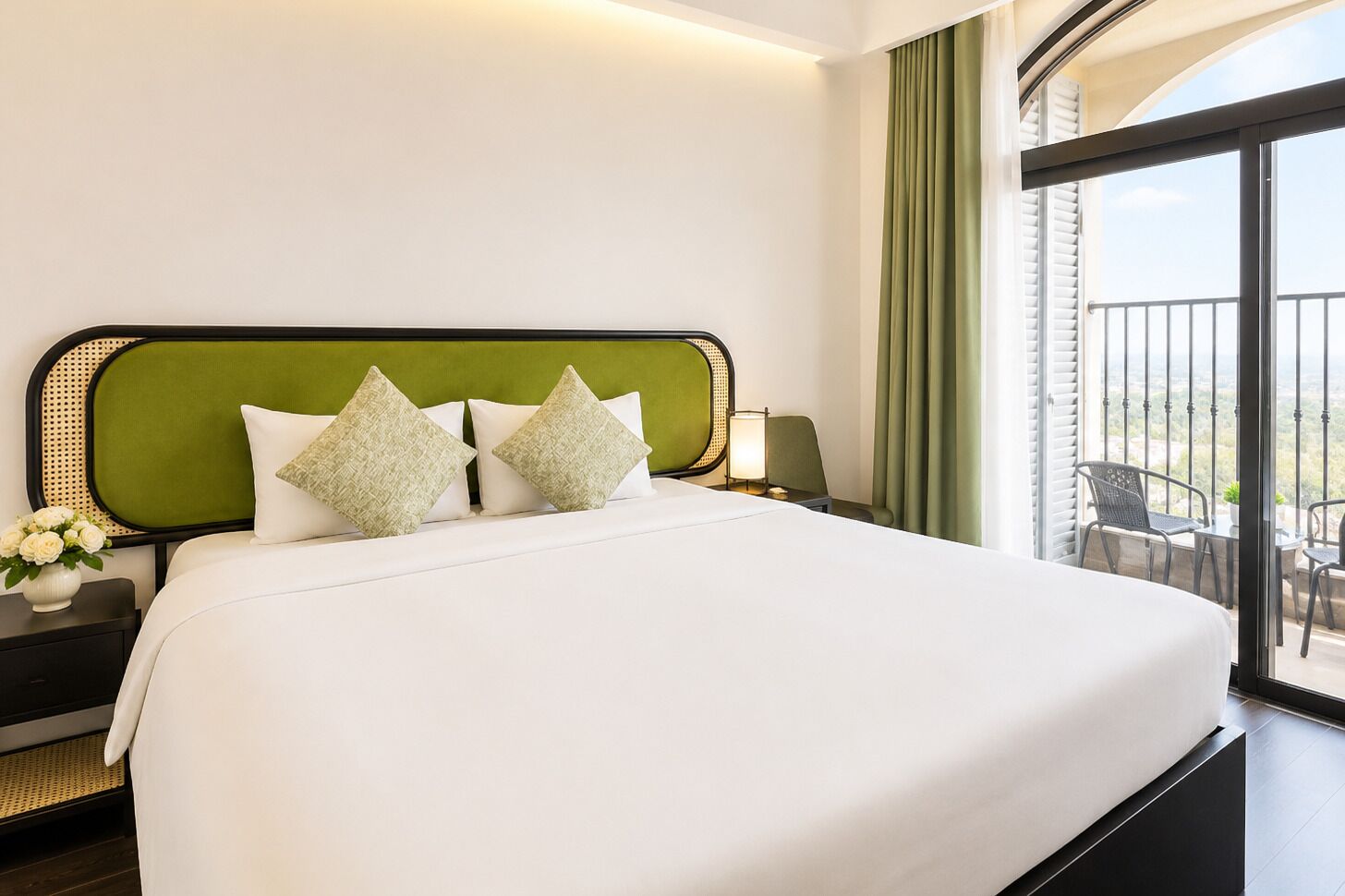 A hotel room with a large bed, a nightstand, a lamp, and a view of the outdoors through a balcony.