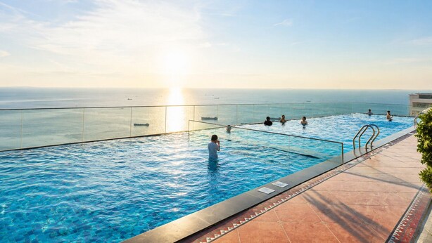 A pool with a view of the ocean, surrounded by a glass barrier and a tiled deck. - Azure Premium Apartments (Phu Quoc)