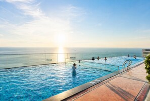 A pool with a view of the ocean, surrounded by a glass barrier and a tiled deck.