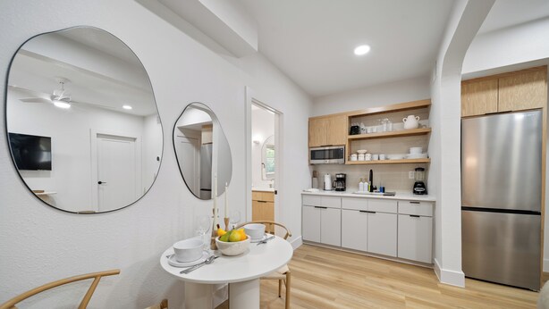 Una cucina moderna con mobili bianchi, un frigorifero in acciaio inossidabile e un'area pranzo con tavolo e sedie bianche.