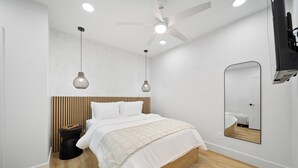 Camera da letto moderna con una testiera in legno, un letto con biancheria bianca, uno specchio rotondo e una ventola a soffitto.