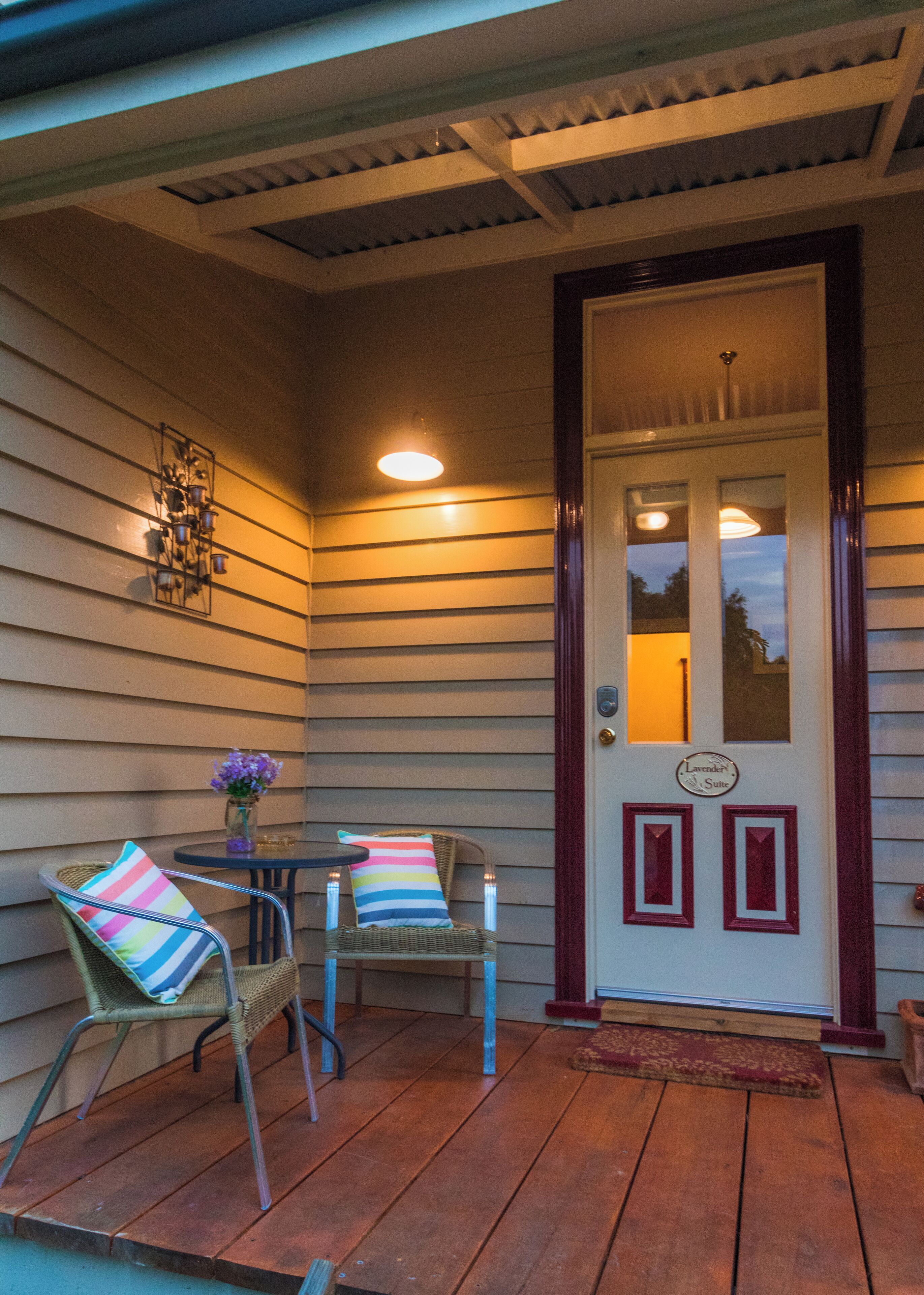 Une véranda avec deux fauteuils en osier, une petite table et un élément décoratif en métal accroché au mur.
