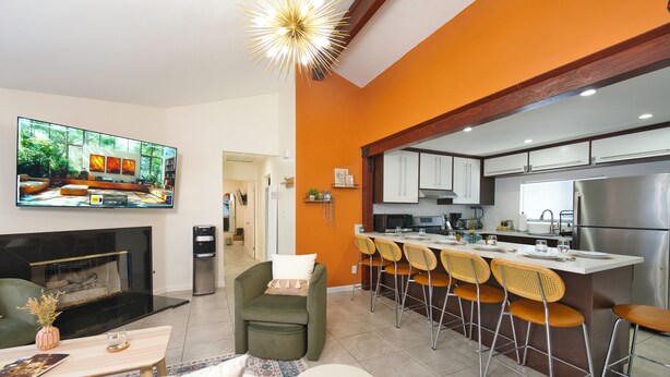 A modern living room with a fireplace, a large flat-screen TV, and a kitchen with bar seating. - Modern Hideaway - Hot Tub + 420 Friendly Patio - Near LAX, Beach + SoFi (Hawthorne)