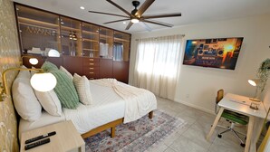 A bedroom with a bed, bedside table, desk, chair, wardrobe, ceiling fan, TV, and a window with curtains. - Modern Hideaway - Hot Tub + 420 Friendly Patio - Near LAX, Beach + SoFi (Hawthorne)
