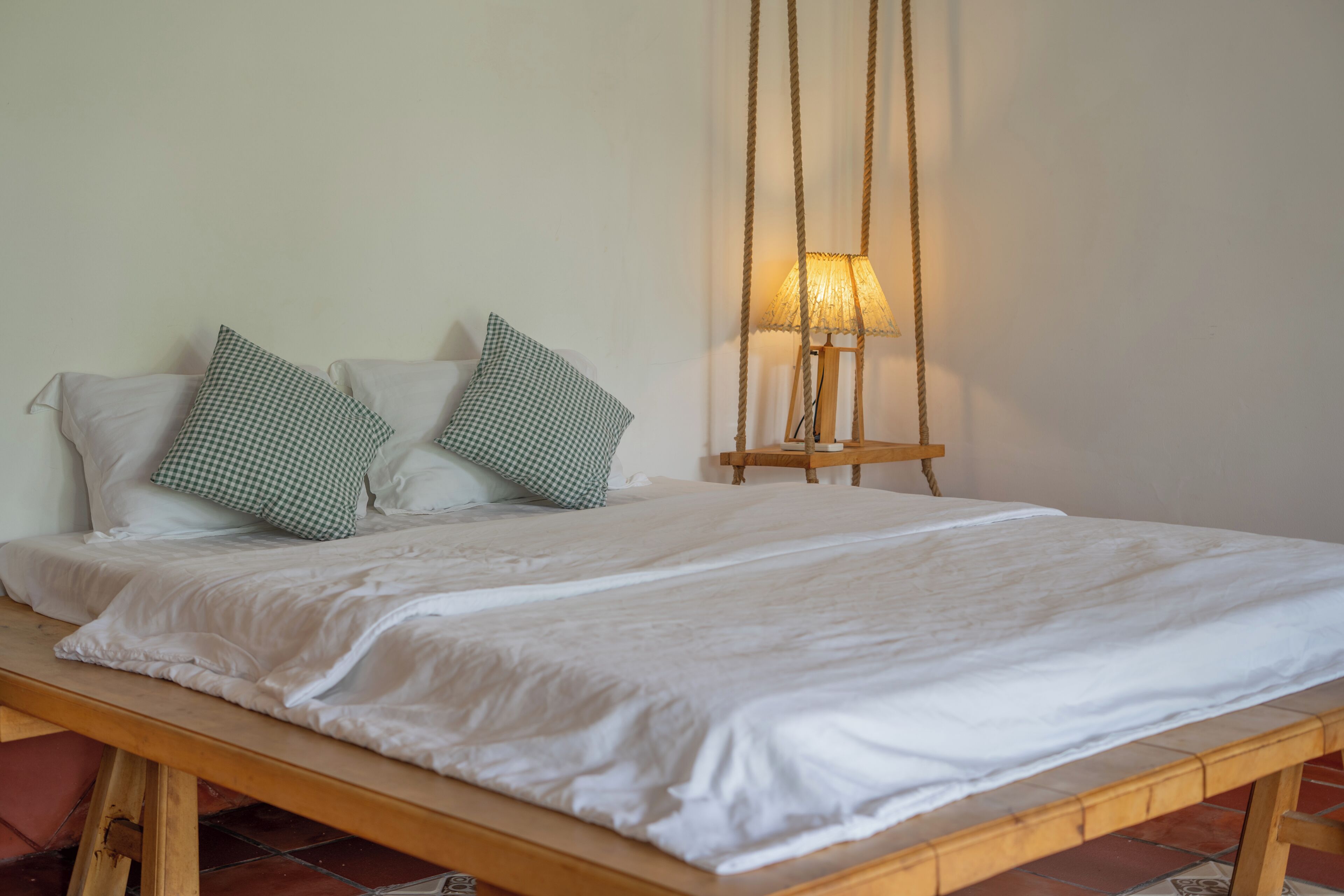 Een bed met witte beddengoed, twee groene geruit kussens en een houten hoofdbord.
