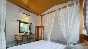 A bedroom with a bed, a small table with chairs, a window, and a mirror. - Bình An Village (Phuoc Hau)