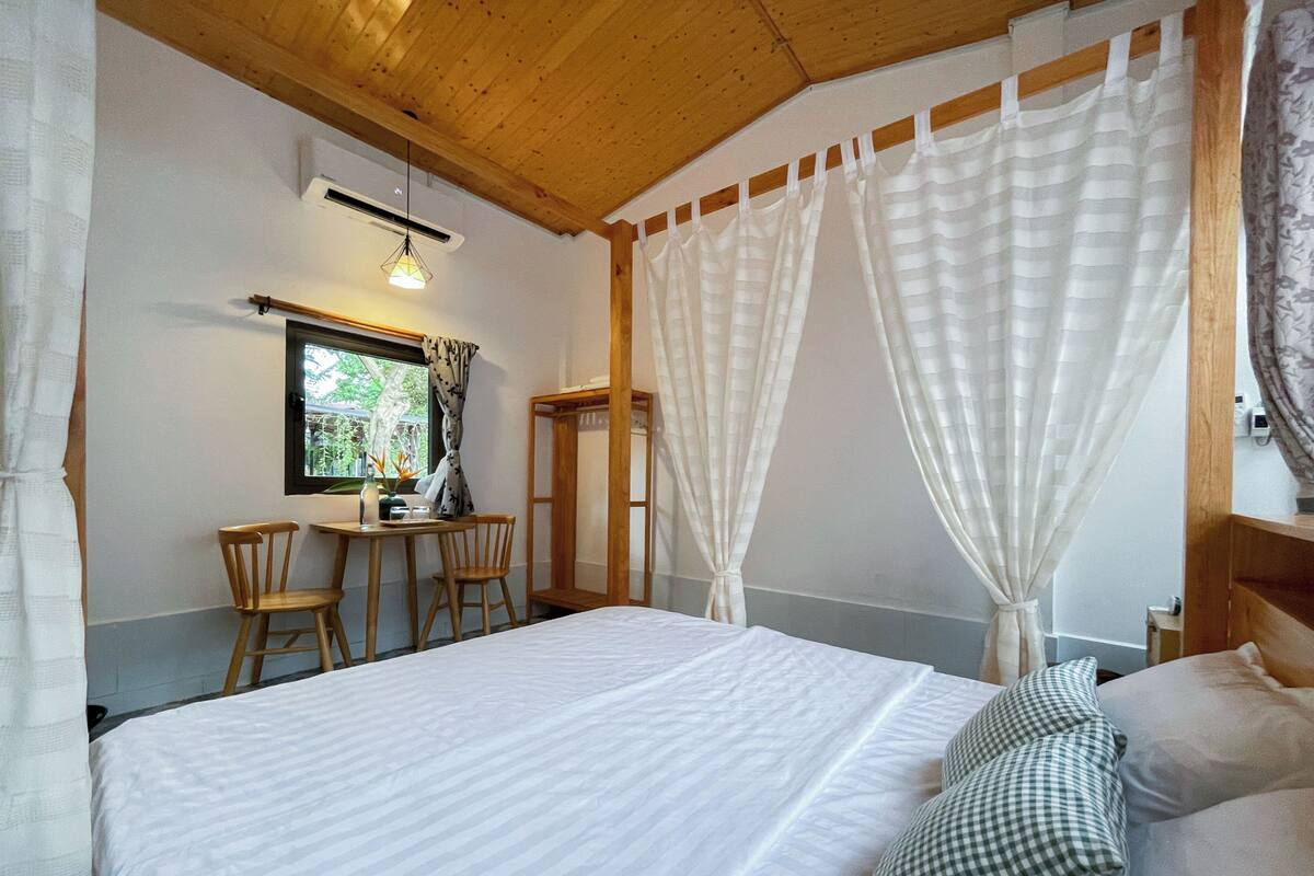 A bedroom with a bed, a small table with chairs, a window, and a mirror.