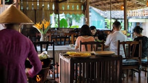 A restaurant with wooden furniture and a thatched roof. - Bình An Village (Phuoc Hau)