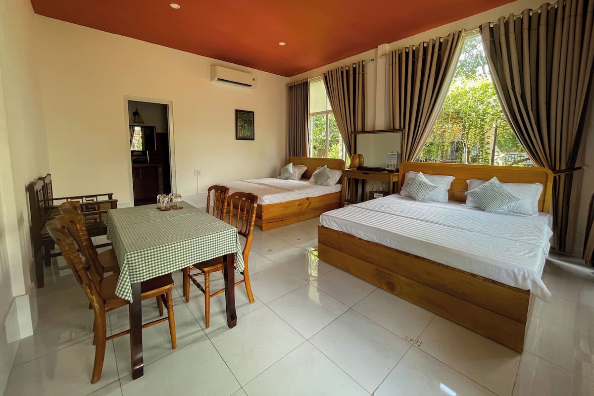 A hotel room with two beds, a dining table, chairs, and a TV.