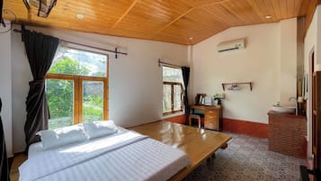 A bedroom with a bed, a desk, a chair, a window with curtains, and a bathroom with a sink and mirror.