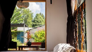 A bedroom with a bed, a window with metal bars, a hanging light fixture, and a view of greenery outside. - Bình An Village (Phuoc Hau)
