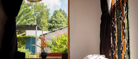 A bedroom with a bed, a window with metal bars, a hanging light fixture, and a view of greenery outside.