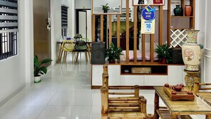 Een moderne eethoek met een houten tafel en stoelen, een decoratieve wand met ingelijste certificaten, en een plafondlamp.