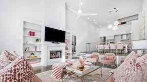Ein modernes Wohnzimmer mit Fernseher, Kamin und Essbereich mit rosa Stühlen.