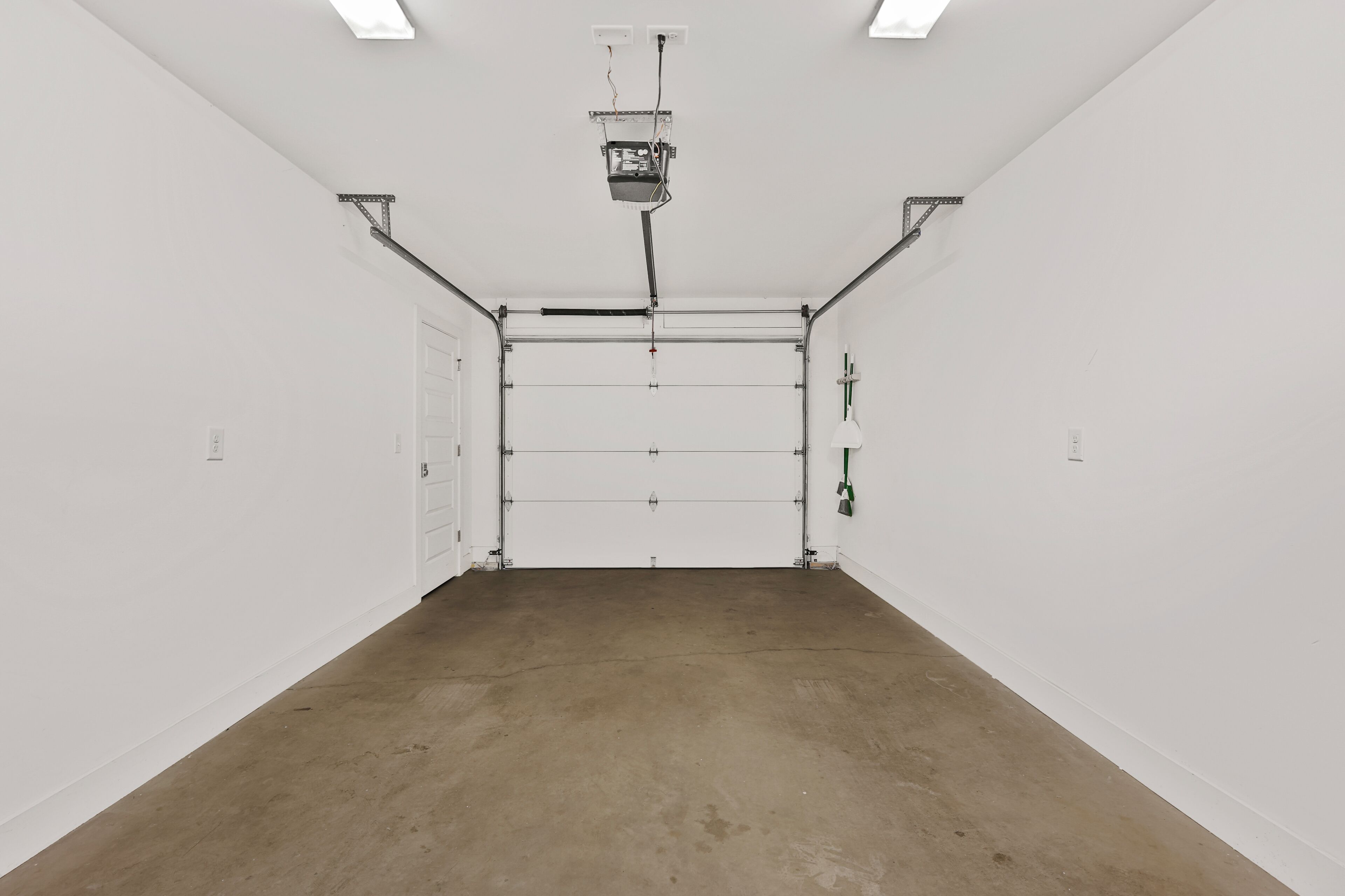 Una habitación amplia y vacía con suelo de hormigón, paredes blancas y una puerta grande de color blanco.