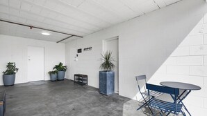 A spacious room with a concrete floor, white brick walls, a small table with chairs, and potted plants. - Bunker 2 "Urban meets Rustic" (Te Awamutu)