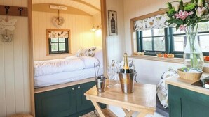 Une pièce chaleureuse avec un lit, une petite table sur laquelle se trouvent une bouteille et des verres, et une fenêtre donnant sur un champ de citrouilles.