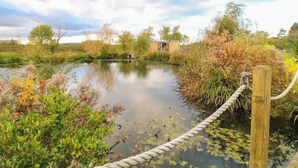 Une scène paisible au bord de la rivière, avec une petite construction en bois, entourée d’une végétation luxuriante et délimitée par une barrière en corde.