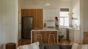 A modern kitchen with wooden cabinets, a stainless steel refrigerator, a central island with stools, and a window overlooking the room. - The River Block (Bookpurnong)
