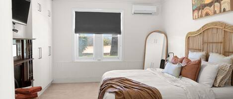 A bedroom with a bed, a TV, a window with a view, and a painting on the wall.