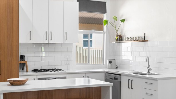 A modern kitchen with white cabinets, a wooden island with stools, a gas stove, a dishwasher, and a window with a view. - The River Block (Bookpurnong)