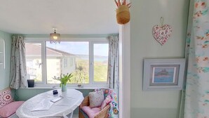 Une pièce chaleureuse avec une table ronde, une chaise en osier et une vue sur une maison par la fenêtre.