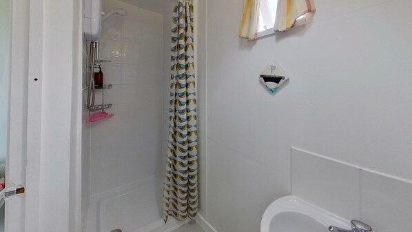 A bathroom with a shower, a toilet, and a small shelf with toiletries.