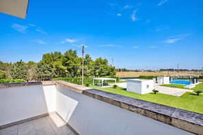 A modern outdoor area with a pool, a covered seating area, and a view of the surrounding landscape.