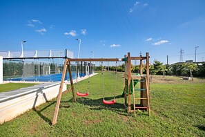 Un parque infantil con columpios y una cancha de tenis cercada.