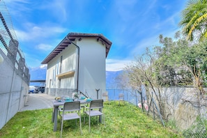 Ein Haus mit weißer Fassade und braunem Dach, ein Tisch mit Stühlen und eine Bergblick im Hintergrund.