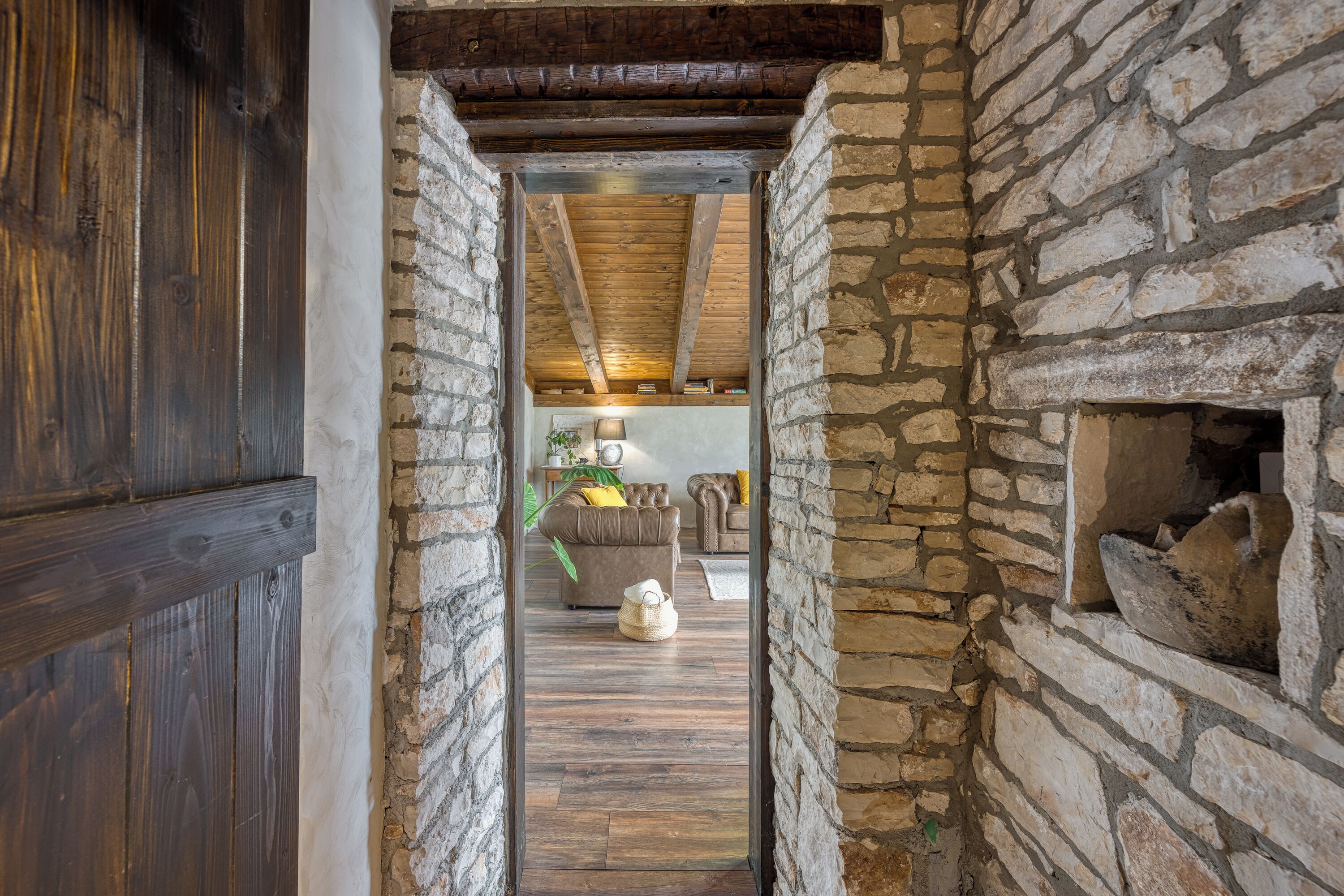 A narrow stone-walled hallway with a wooden door and ceiling beams.