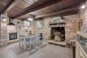 A rustic kitchen with stone walls, a wooden ceiling, and a central fireplace.