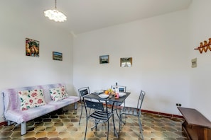 A dining area with a table set for four, a sofa, and a hanging light fixture.