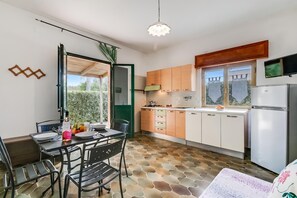 A compact kitchen with a dining area, a refrigerator, and a television mounted above the counter.