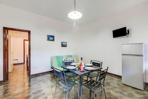 A dining area with a table set for two, a refrigerator, and a television mounted on the wall.