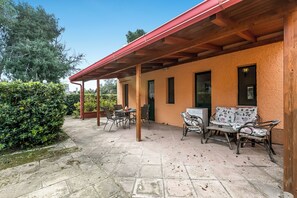 An outdoor patio with stone flooring, wooden pergola, and wicker furniture.