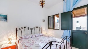 A bedroom with a bed, a nightstand, a lamp, a window with curtains, and a view of the outside.