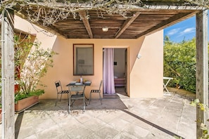 Un patio con mesa y sillas, una pérgola de madera y vistas a un jardín.