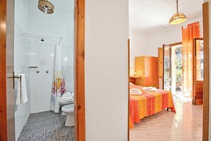 A bathroom with a shower, toilet, and a bed with a colorful bedspread.