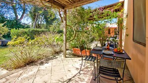 Une terrasse couverte avec une table dressée pour le repas, entourée de plantes en pot et d’arbres.
