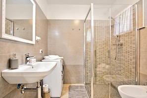 Un baño moderno con un lavamanos grande, una lavadora, ducha con puertas de vidrio y un espejo.