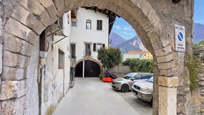 Una calle estrecha con un arco de piedra, un edificio con un portón negro y un cartel que indica zona de estacionamiento prohibido.