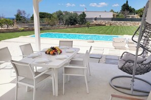 An outdoor dining area with a pool, white furniture, and a hanging chair.