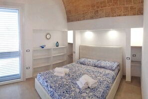 A bedroom with a bed, built-in shelving, a window with blinds, and a brick ceiling.