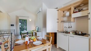 A compact kitchen with white cabinets, a dining table set with plates, a bottle, and fruits. - Borgo Primizia M4 Pool And Sea, Otranto, Italy (Otranto)