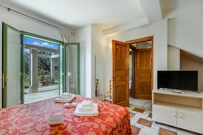 A bedroom with a bed, a TV, a wooden door, and a view through a glass door.