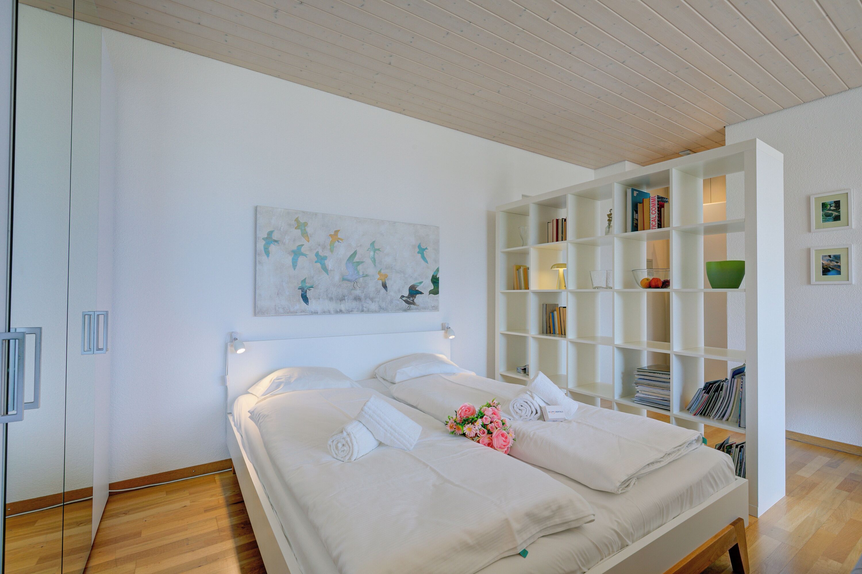 Un dormitorio moderno con una cama grande, un armario blanco y una estantería empotrada.